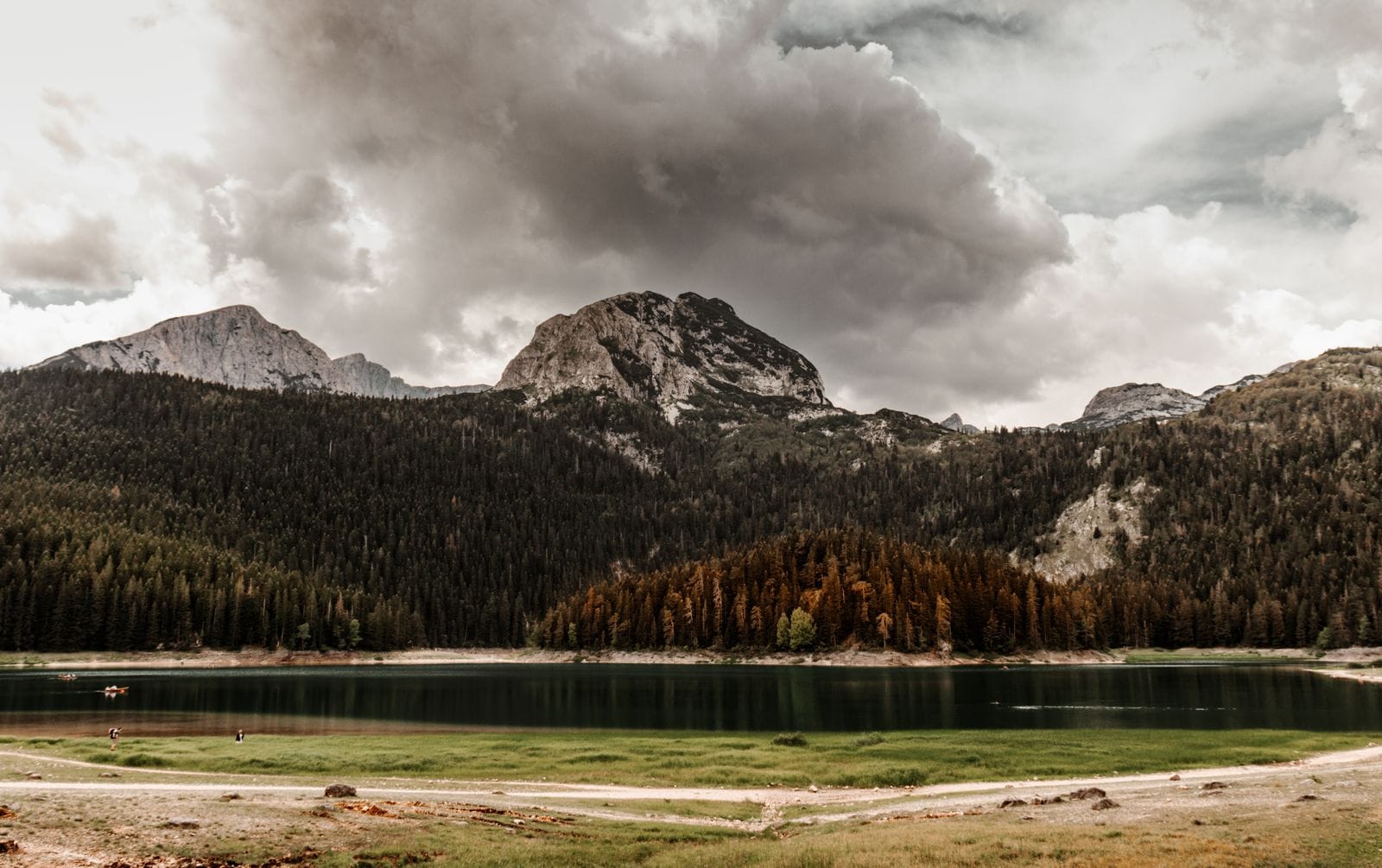 The Black Lake in Durmitor National Park with dark pine forest along the shore and a bare mountain peak under heavy cloud