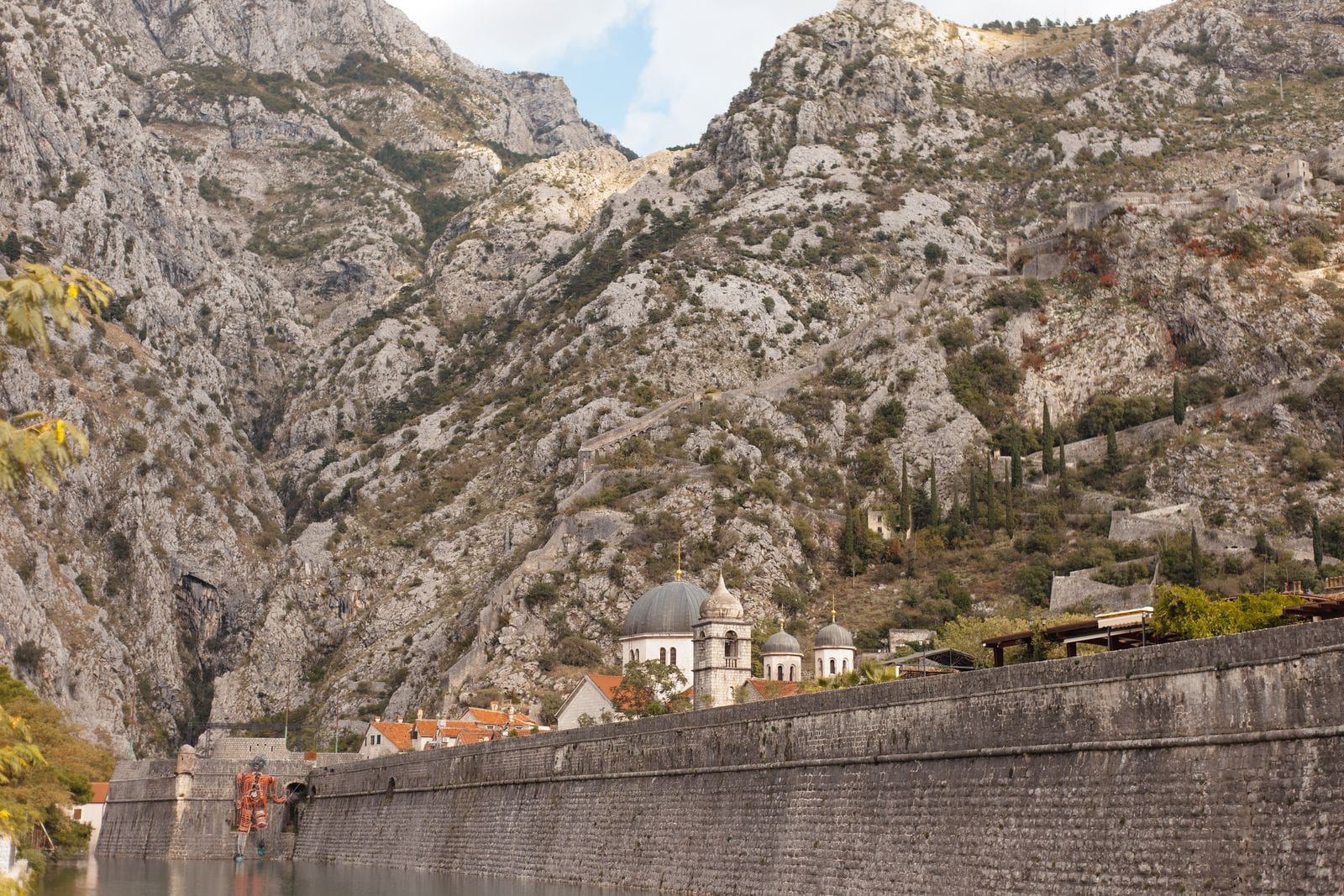 The stone fortification wall of Kotor climbing a steep rocky mountainside above the red roofs of the old town