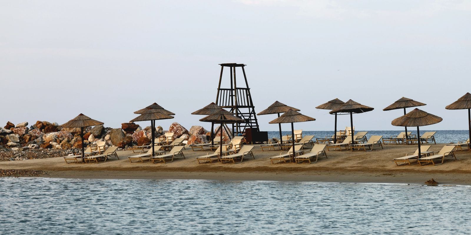 Rows of wooden sunbeds and straw umbrellas on an organised Mediterranean beach