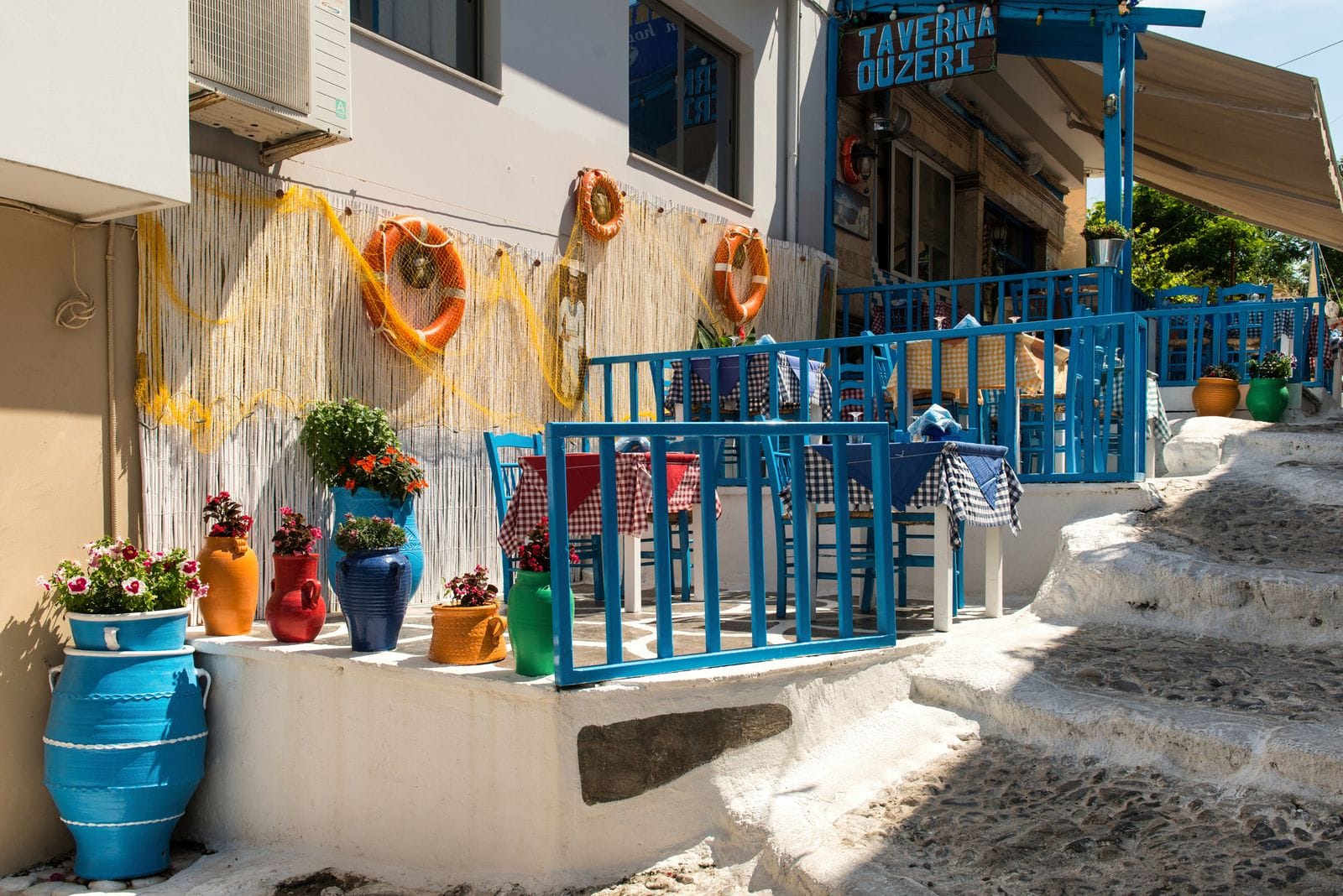 A traditional Greek taverna with blue painted chairs, potted plants and a menu board outside