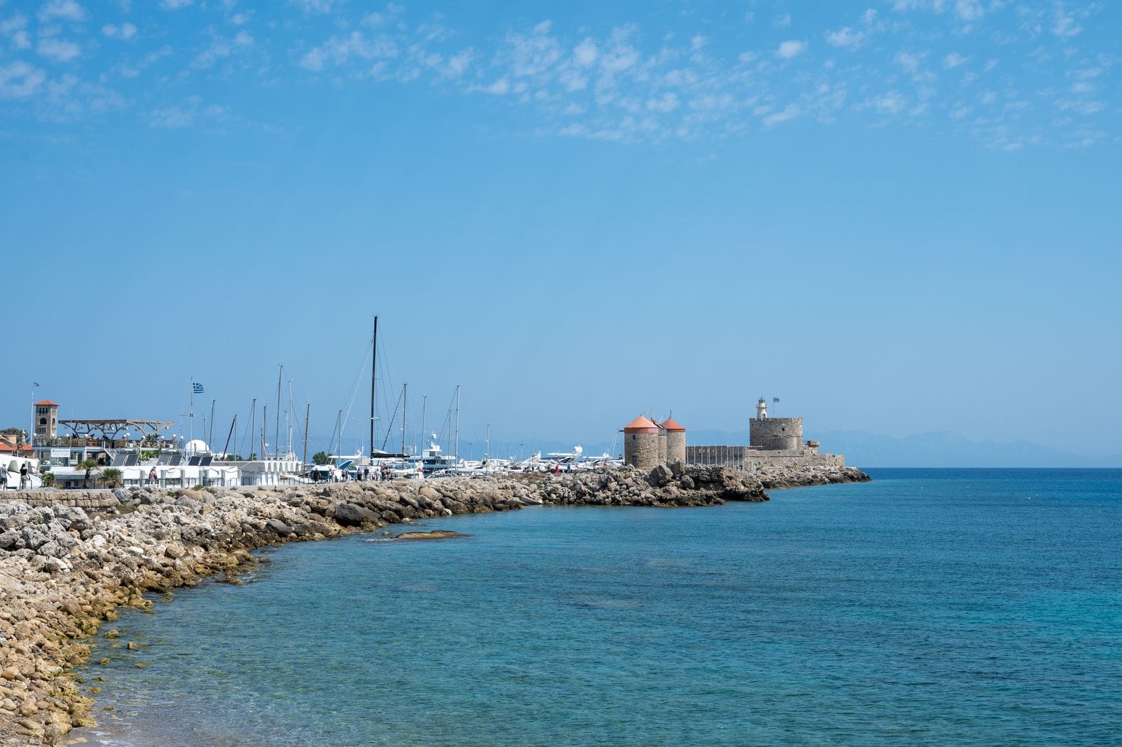 Mandraki harbour in Rhodes with the stone windmills and Fort St Nicholas on the breakwater