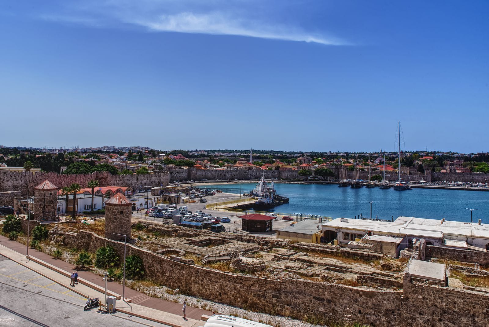 Is Rhodes expensive: the harbour and medieval town walls of Rhodes Town from above under a clear blue sky