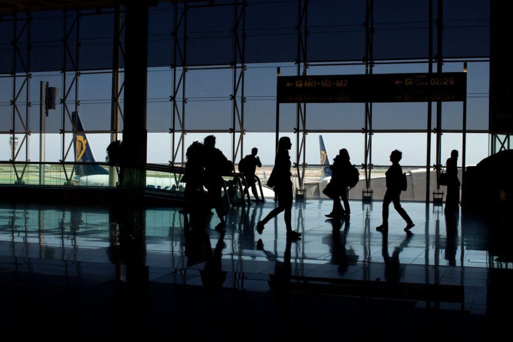 Ryanair airport check in: silhouettes of passengers walking through an airport terminal, with an aircraft visible through the window