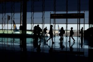Ryanair airport check in: silhouettes of passengers walking through an airport terminal, with an aircraft visible through the window