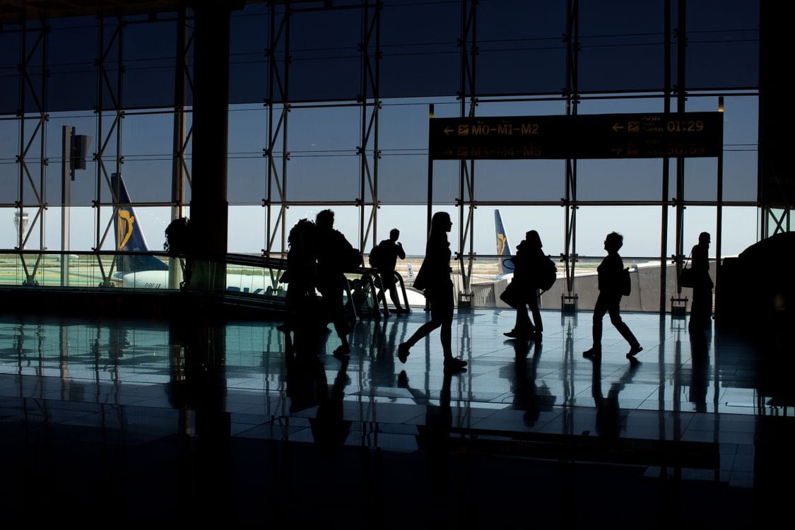 Ryanair airport check in: silhouettes of passengers walking through an airport terminal, with an aircraft visible through the window