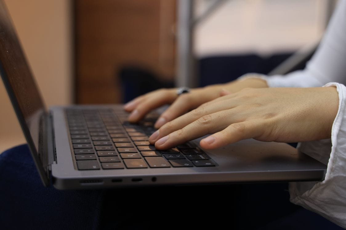 Close-up of hands typing on a laptop keyboard while sat down