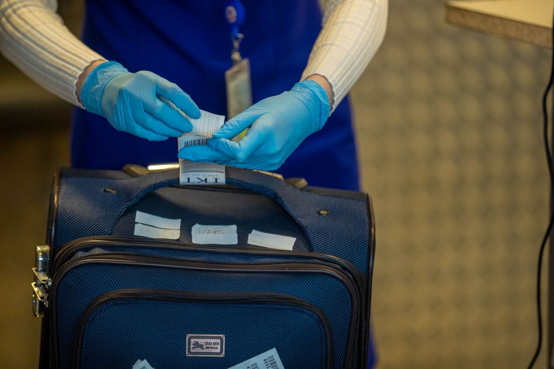 Ryanair liquids rules in action: an airport worker's gloved hands checking and tagging a passenger's suitcase