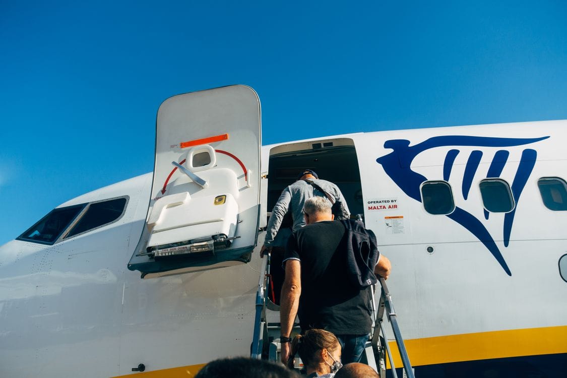 A passenger climbing the steps to board a Ryanair aircraft, the tail logo visible above the door