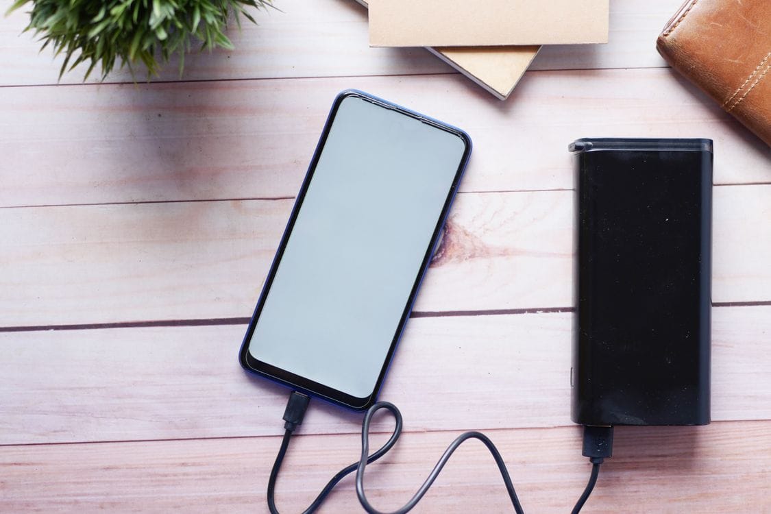 A smartphone charging from a power bank on a wooden desk