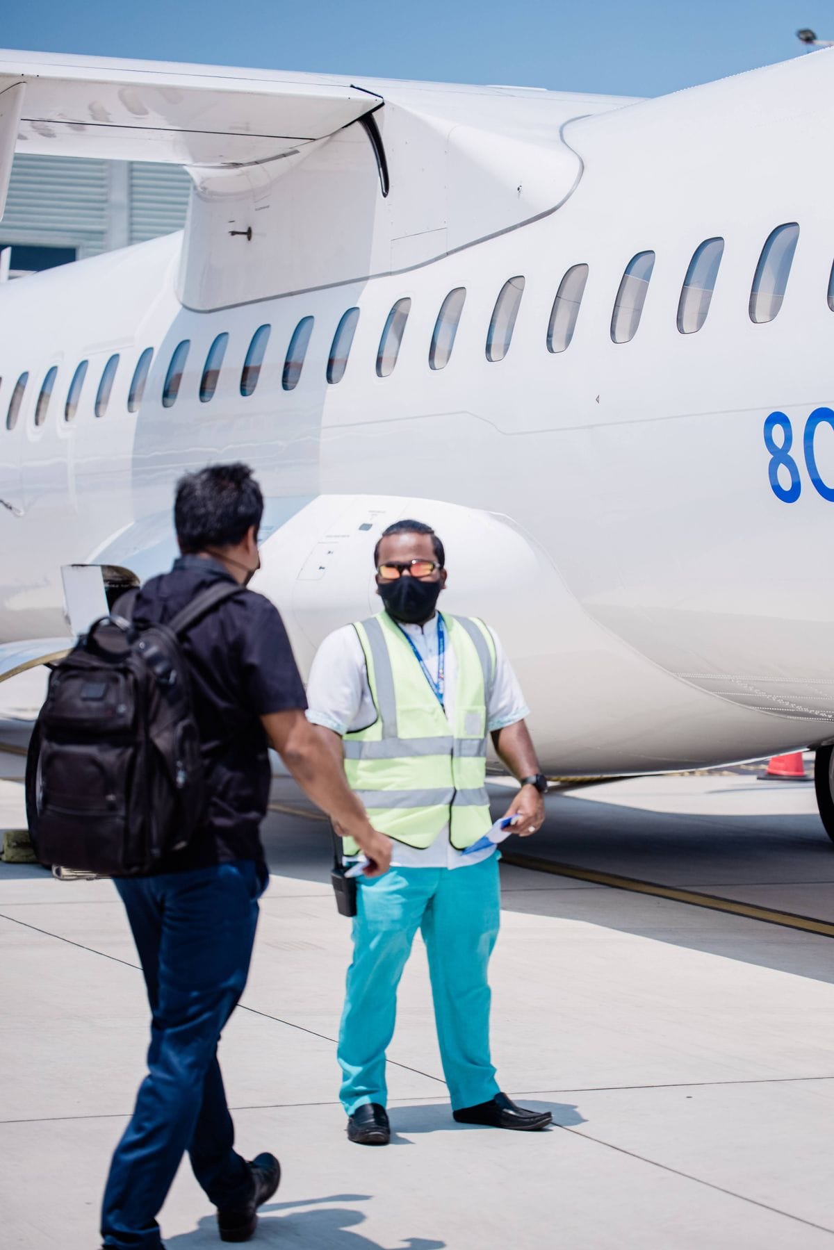 A member of airport ground staff meets a passenger on the tarmac beside an aircraft