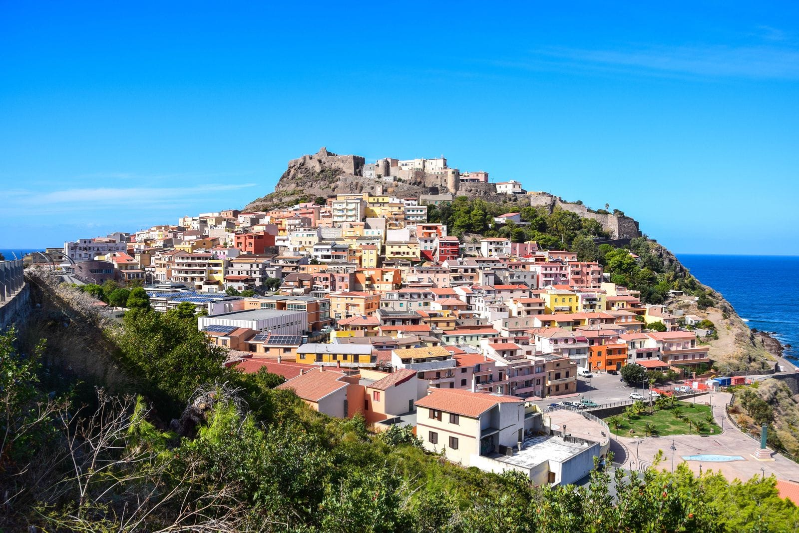 The pastel-coloured houses of Castelsardo stacked up a headland below its medieval castle, with the sea to the right