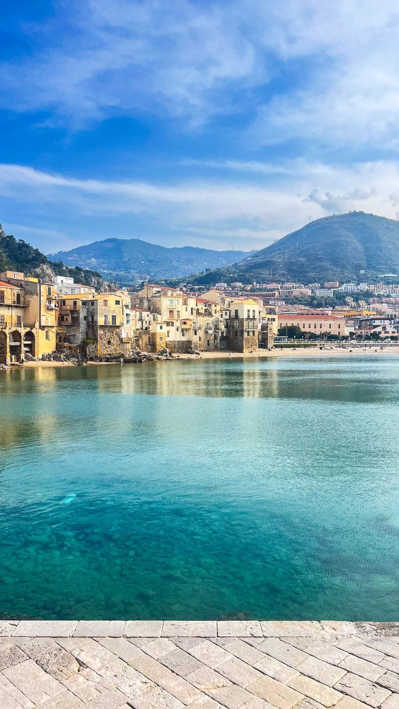 Cefal&ugrave;'s old town rising directly from turquoise water, mountains behind