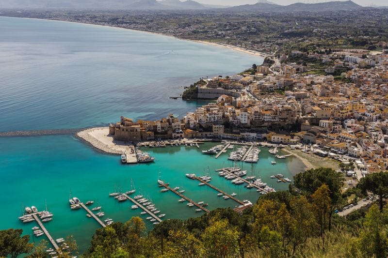 Sicilian harbour town with a working marina and pastel old-town buildings on the water