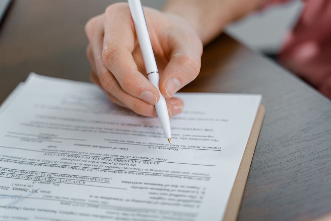 A hand holding a pen, signing a compensation claim document