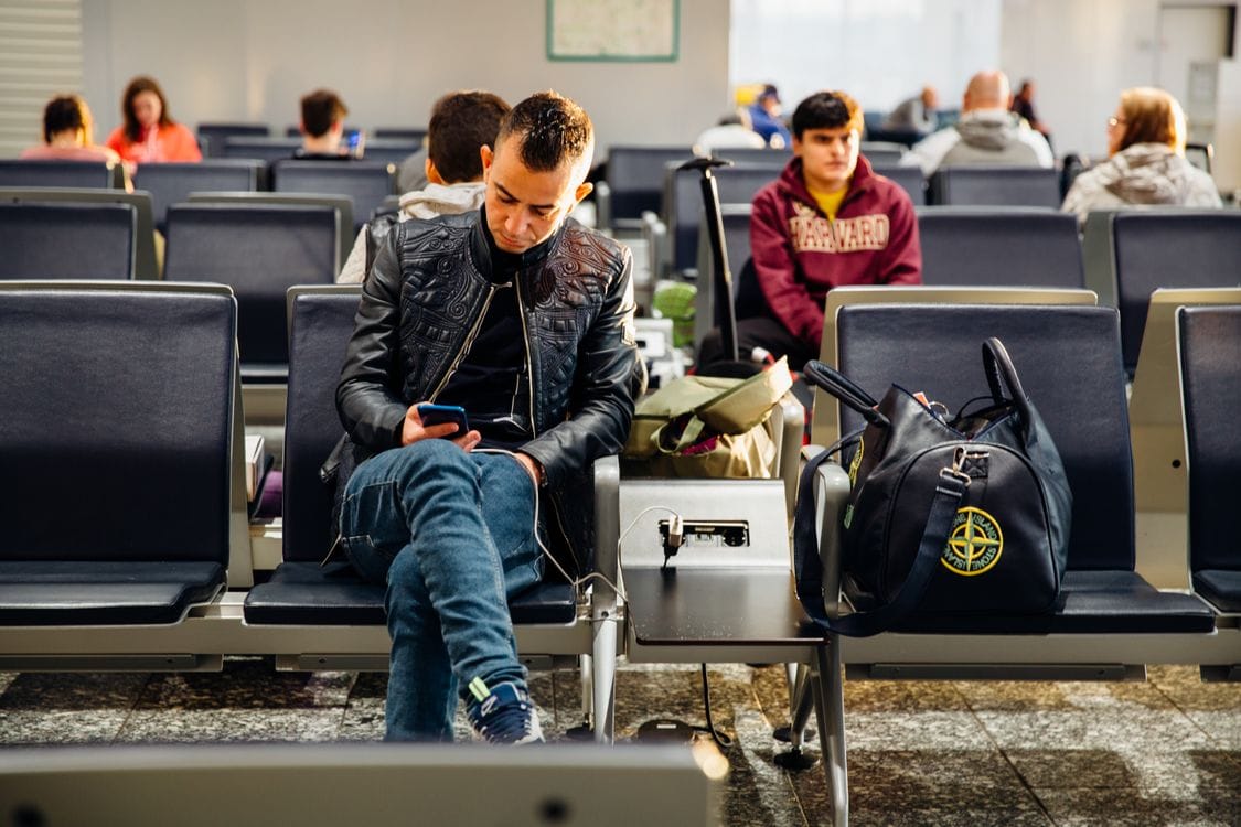 Passengers sitting in an airport lounge on their phones while they wait