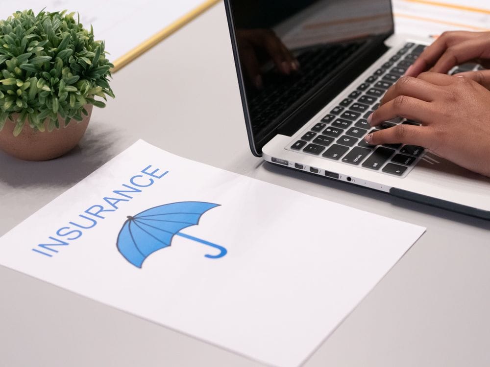 Hands typing on a laptop next to an insurance document on a desk