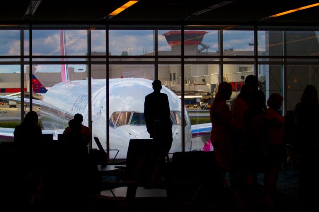 How strict is Wizz Air with hand luggage: silhouettes of passengers waiting at an airport departure gate with an aircraft visible through the window