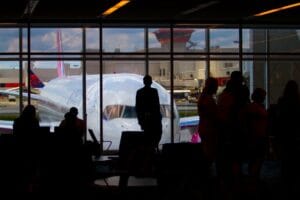 How strict is Wizz Air with hand luggage: silhouettes of passengers waiting at an airport departure gate with an aircraft visible through the window