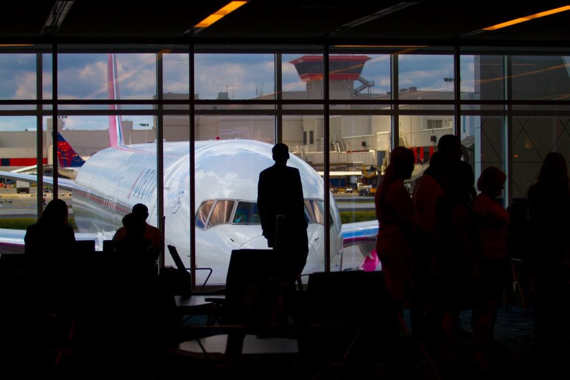 How strict is Wizz Air with hand luggage: silhouettes of passengers waiting at an airport departure gate with an aircraft visible through the window