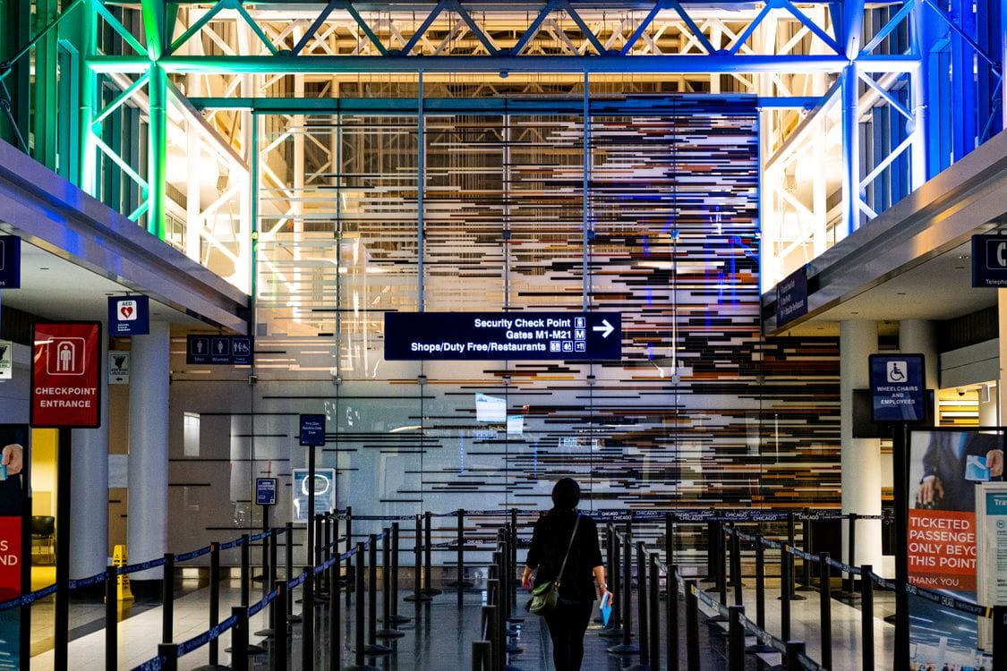 A passenger walking through an empty airport security checkpoint walkway towards the departure gates