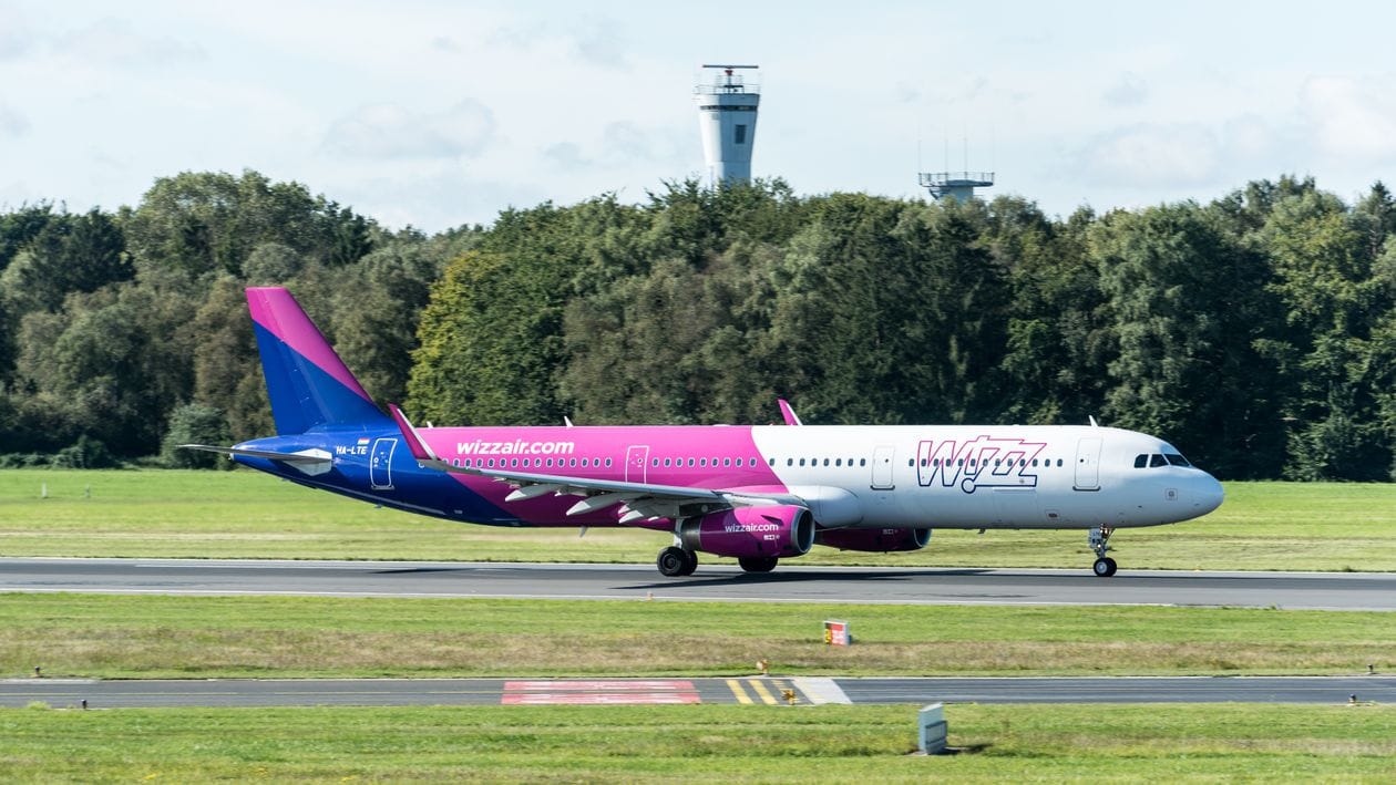 A Wizz Air Airbus A321 taxiing at an airport with the control tower in view