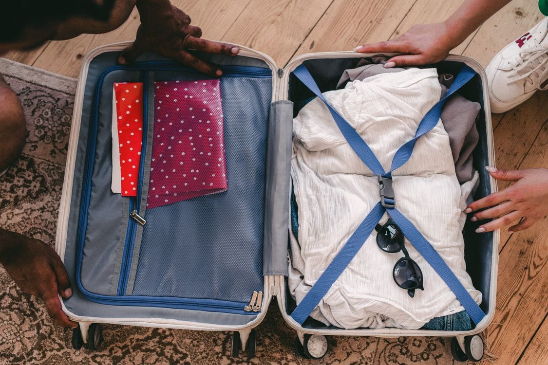 An open suitcase packed with folded clothes and sunglasses, ready for a trip