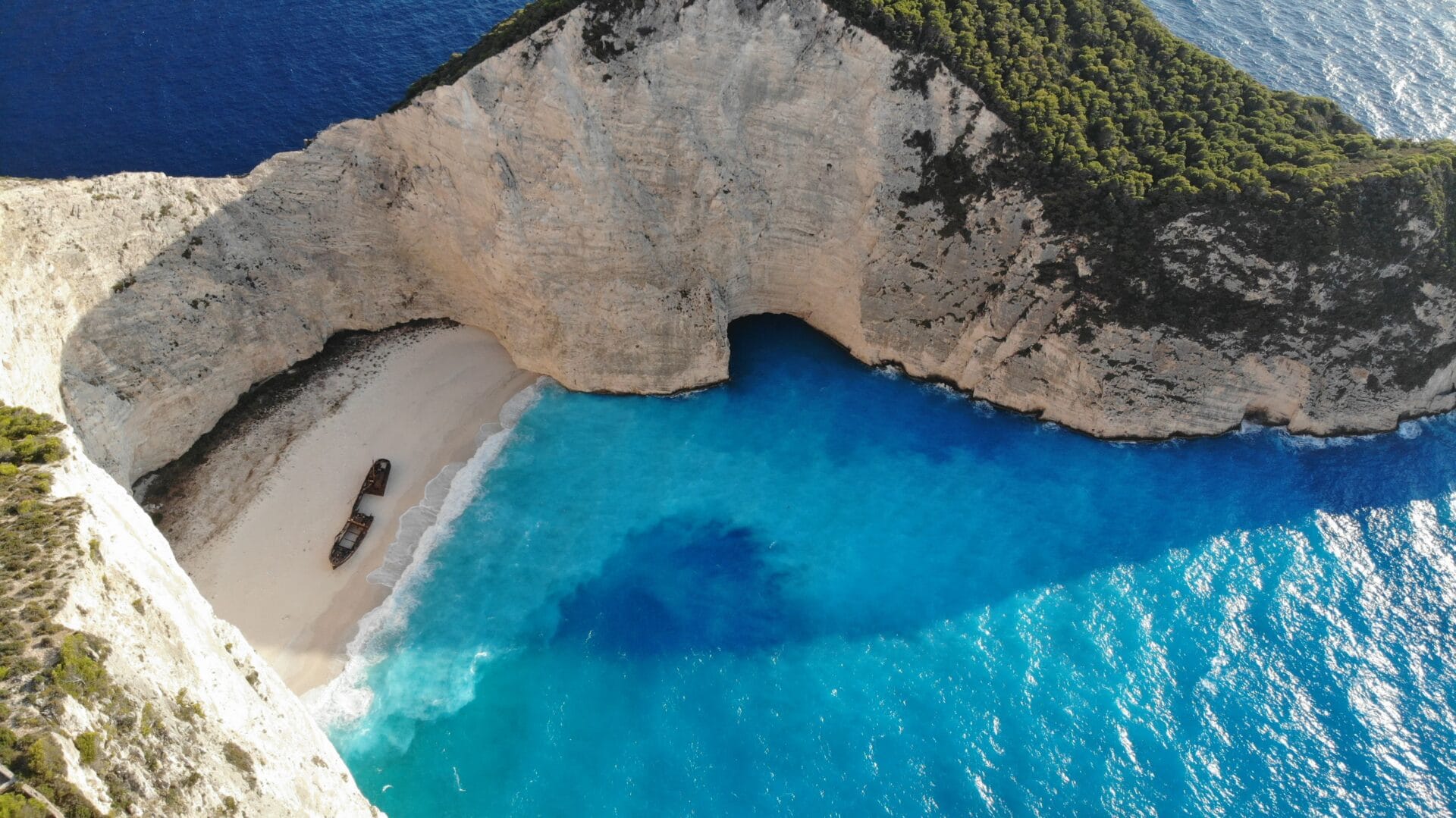 Aerial view of Navagio Shipwreck Beach on Zakynthos, a rusting wreck on white sand ringed by limestone cliffs and turquoise sea