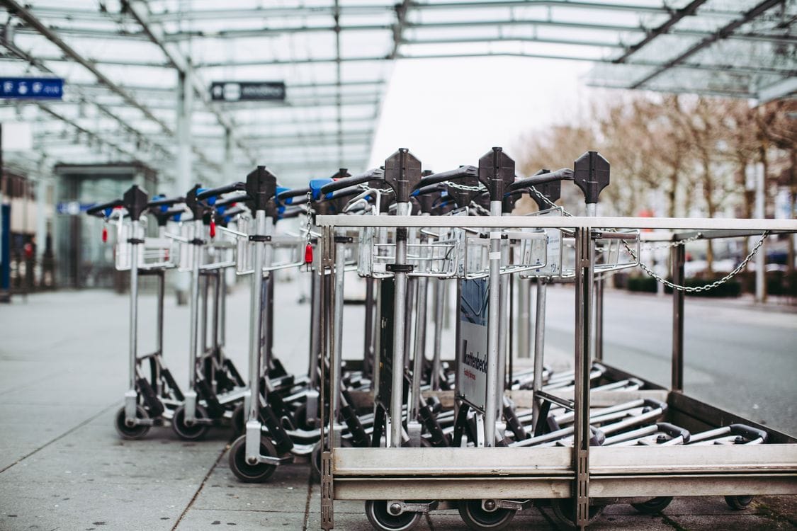 Luggage trolleys lined up outside an airport terminal under a glass canopy