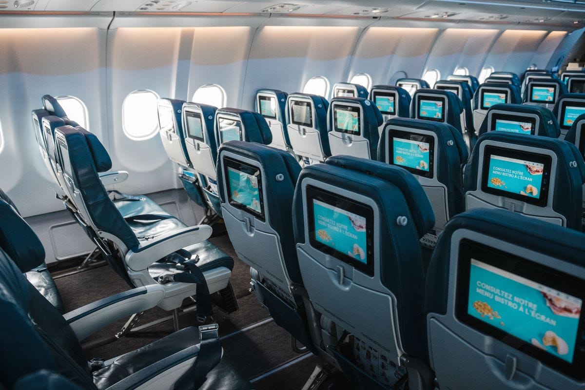 Rows of empty airline seats with individual touchscreens in an aircraft cabin