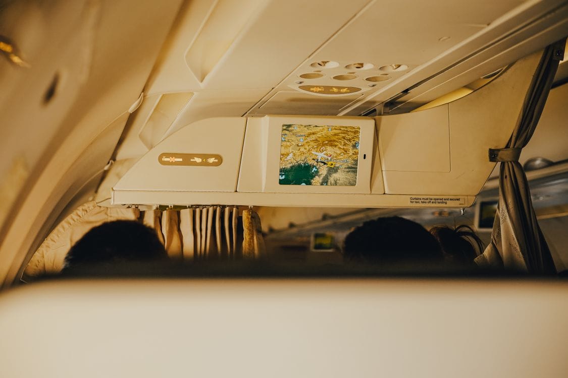 An overhead in-flight map screen glowing inside an airplane cabin