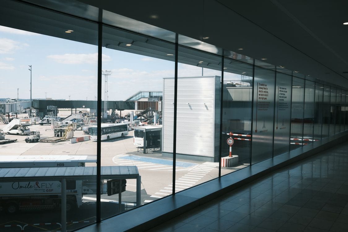 An empty airport corridor with floor-to-ceiling windows looking out over parked buses and the apron