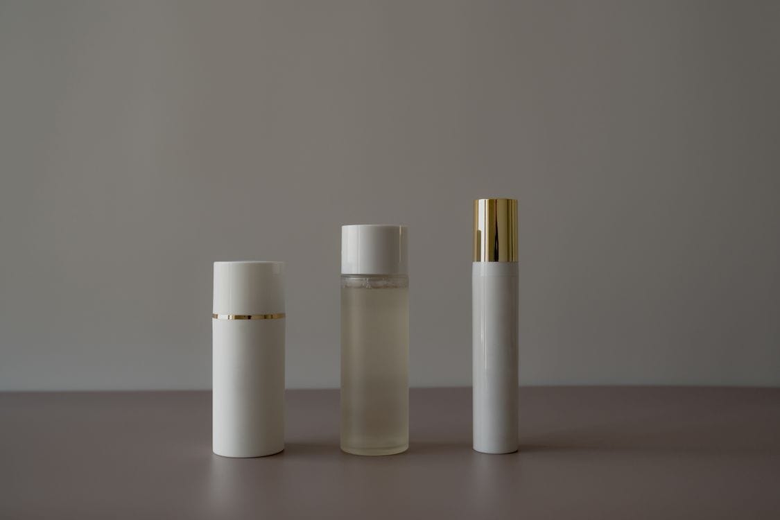 Three white cosmetic bottles of different heights lined up on a pale surface