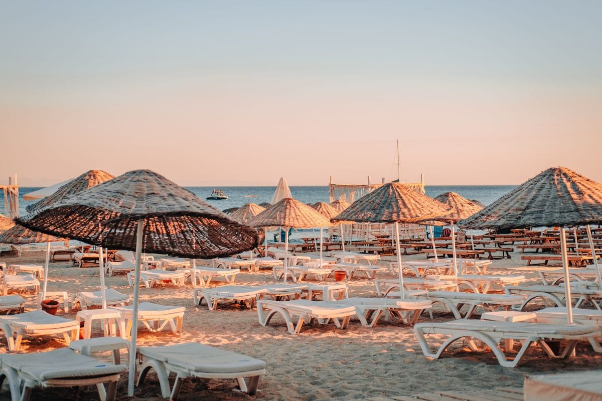 Rows of empty sun loungers and straw umbrellas on a Mediterranean beach at golden hour
