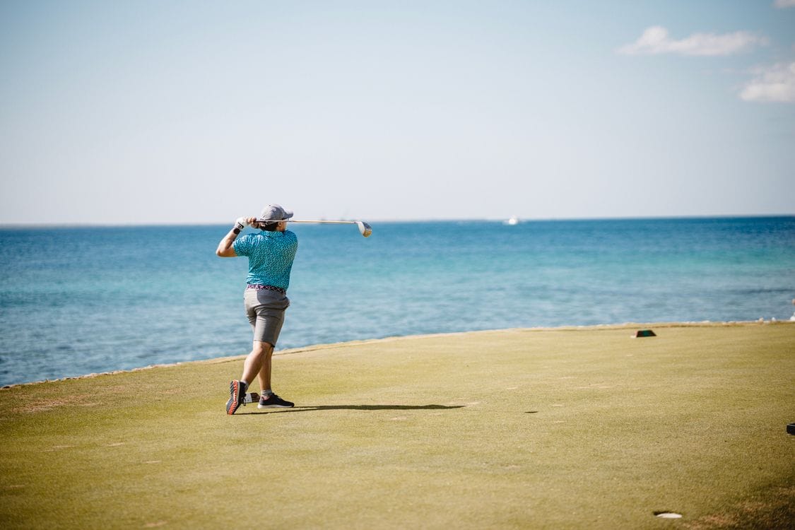 A man playing golf on a course beside the sea