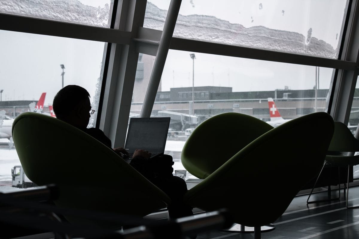 Someone using a laptop in an airport lounge, silhouetted against the window