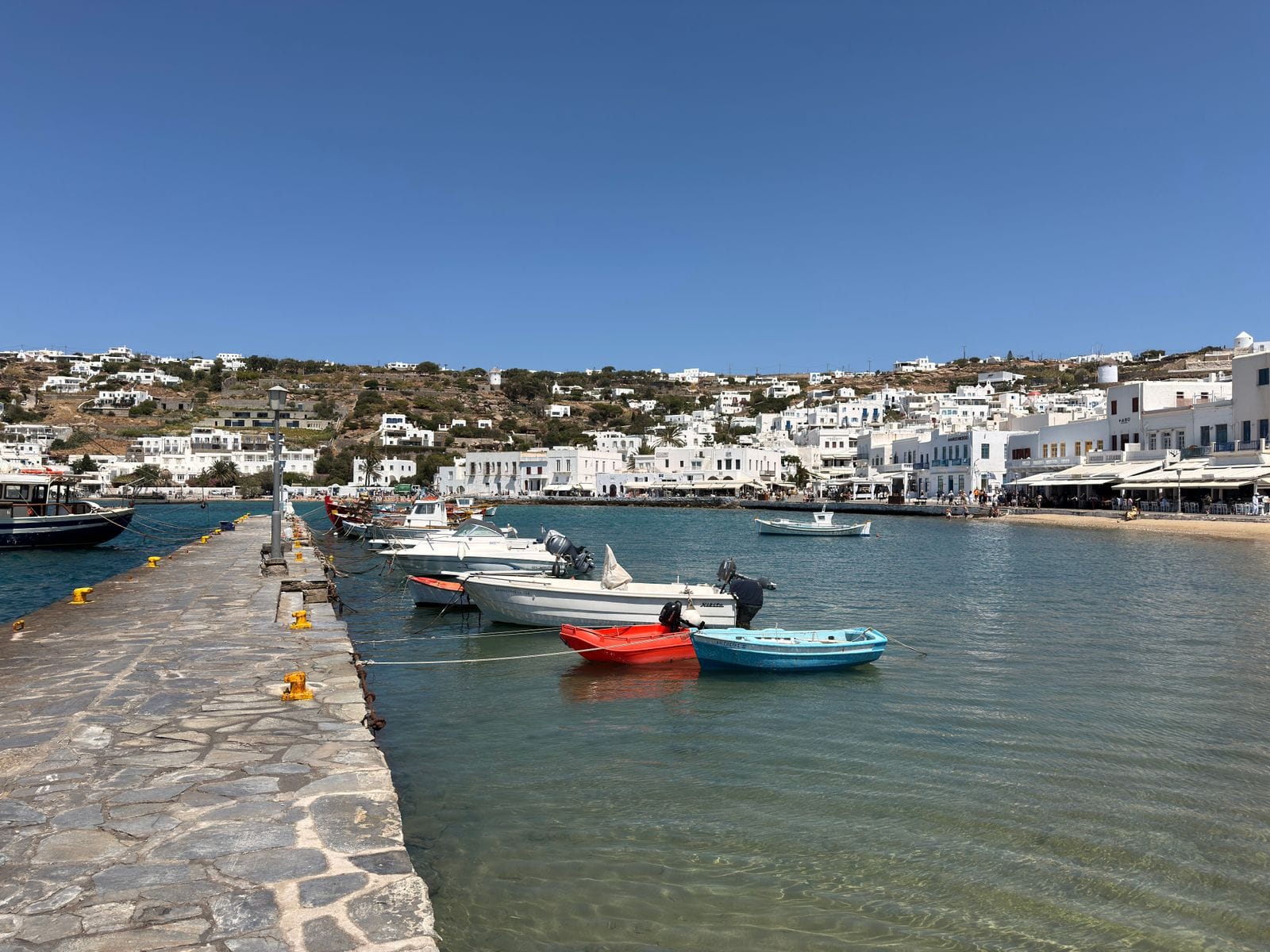 Small fishing boats moored in Mykonos harbour with the whitewashed town behind, under a clear sky