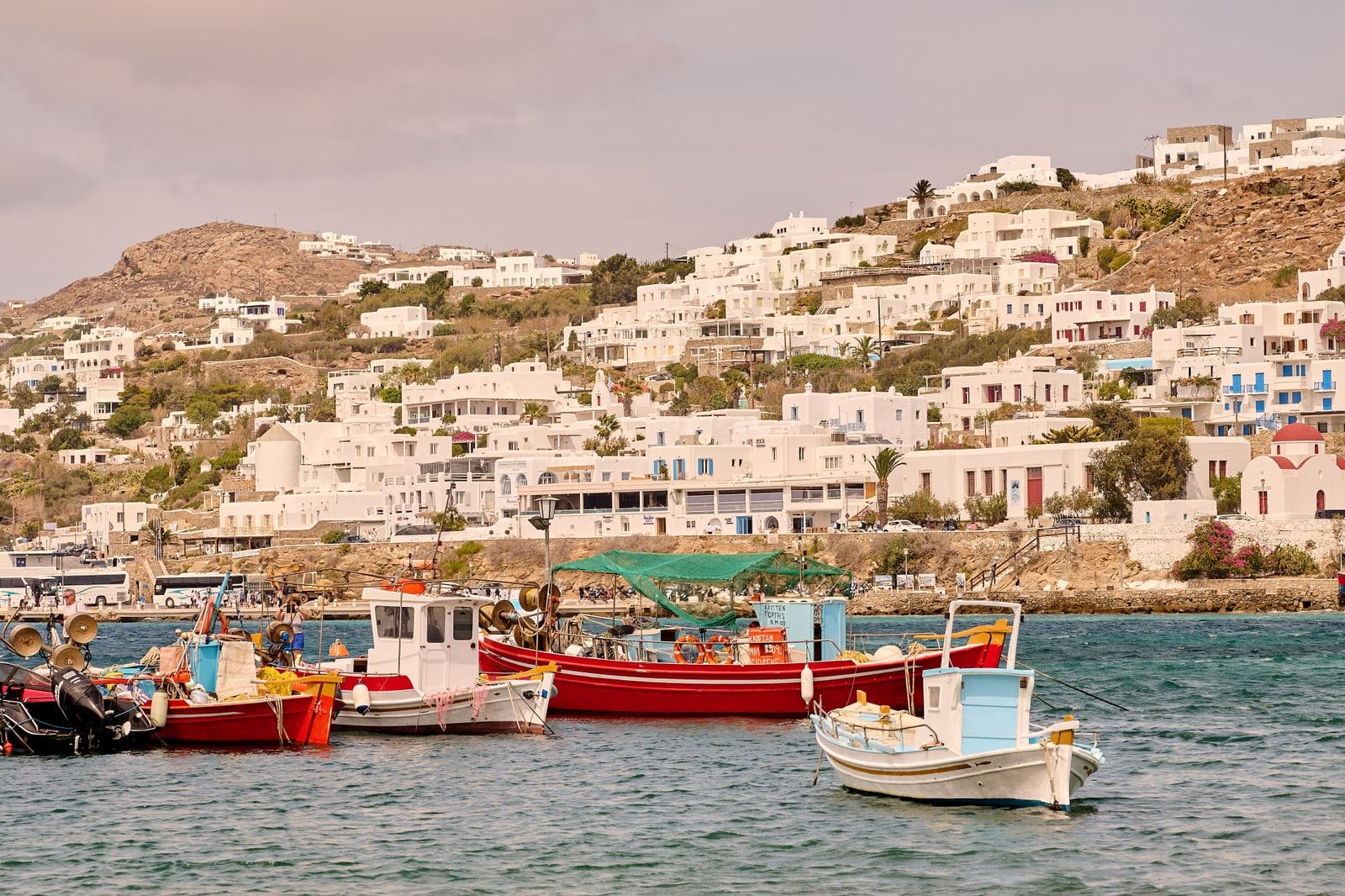 Colourful traditional fishing boats moored in Mykonos harbour with the whitewashed hillside town behind