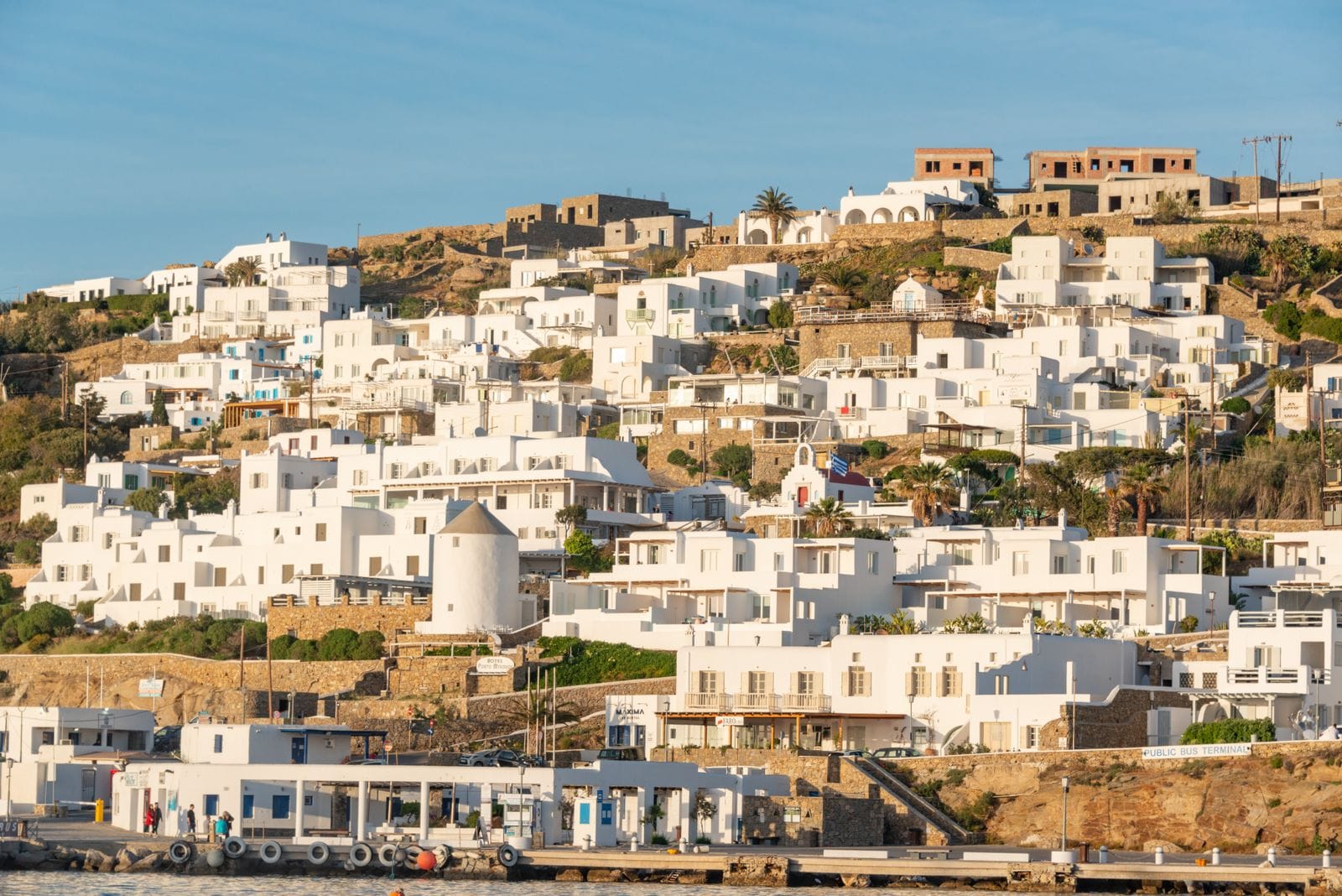 Traditional white Cycladic houses covering a hillside above Mykonos harbour, seen from the water