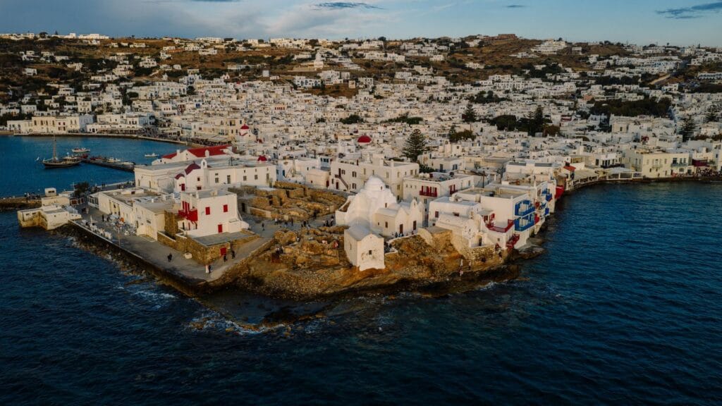 Is Mykonos expensive: aerial view of Mykonos Town's whitewashed buildings on the headland, harbour boats in the water