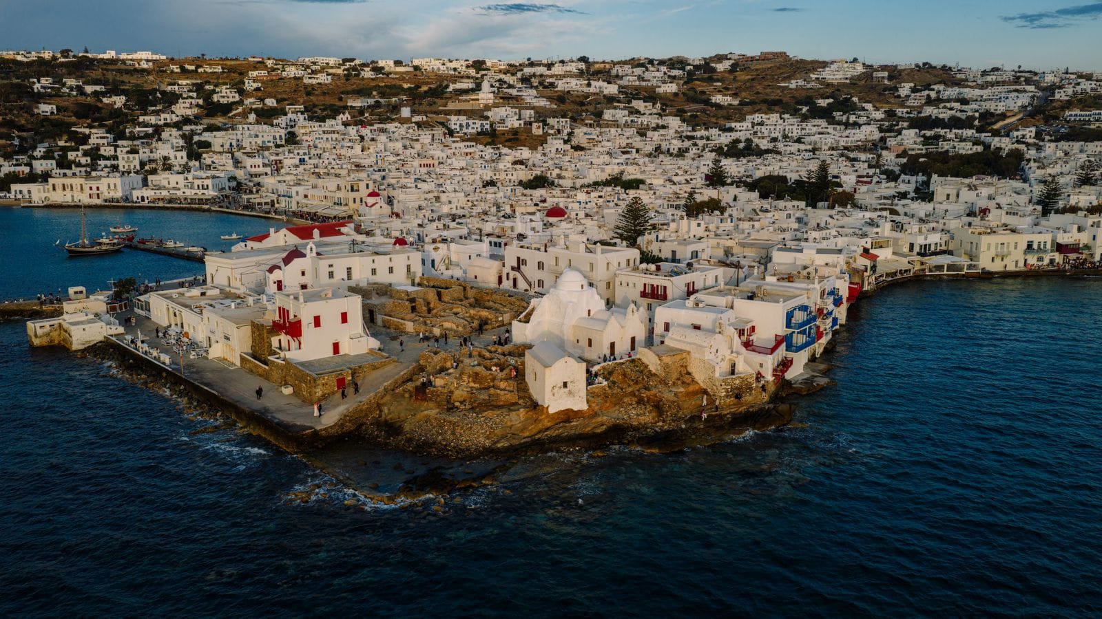 Is Mykonos expensive: aerial view of Mykonos Town's whitewashed buildings on the headland, harbour boats in the water