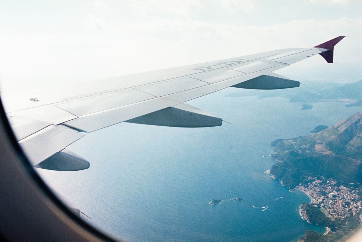 A plane wing seen from the cabin window, over a Mediterranean coastline