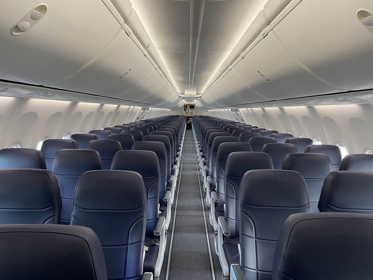 Empty economy aircraft cabin with rows of dark blue seats stretching to the rear exit