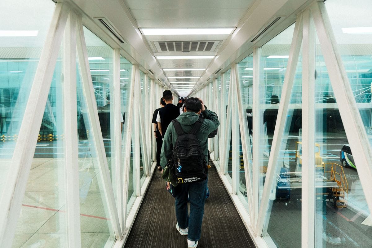 Travellers with backpacks walking through a glass jet bridge towards their aircraft