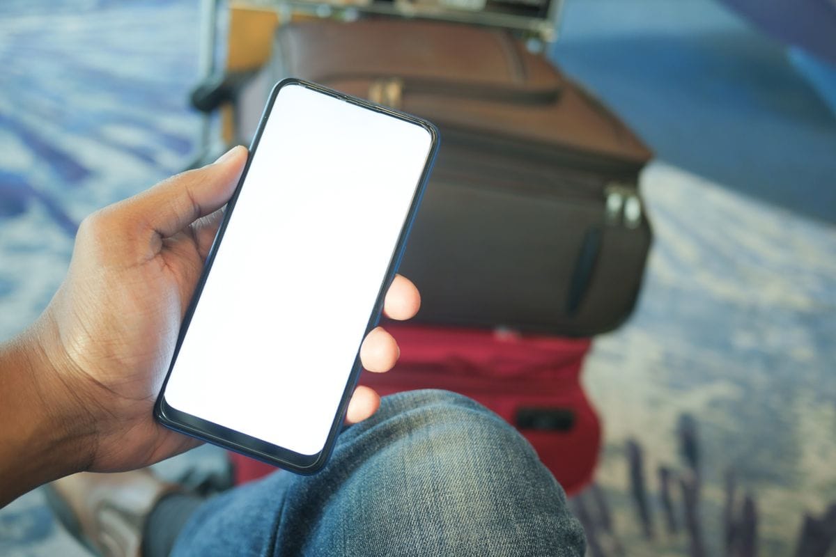 A smartphone held up at an airport, with a suitcase in the background