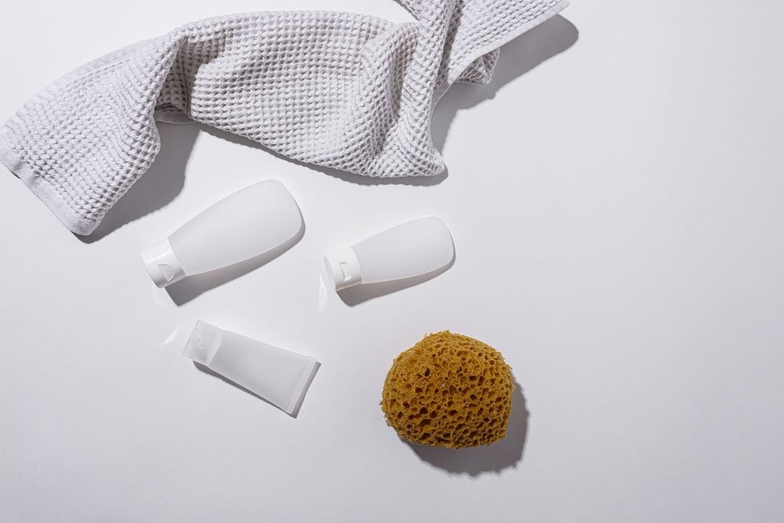 TUI liquid rules: three white travel-size tubes and bottles beside a natural sponge and a waffle towel