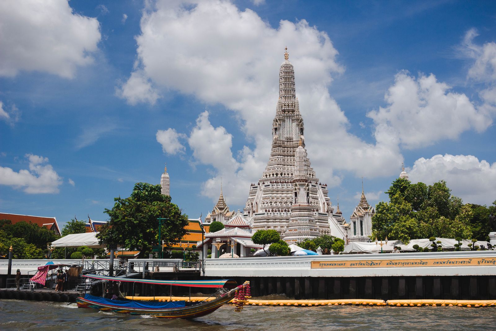 Wat Arun temple on the Chao Phraya River in Bangkok, with a boat on the water under a blue sky