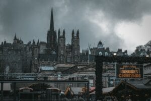 Best Christmas markets in the UK: the Edinburgh's Christmas sign beside market stalls, below the Old Town spires under a grey sky