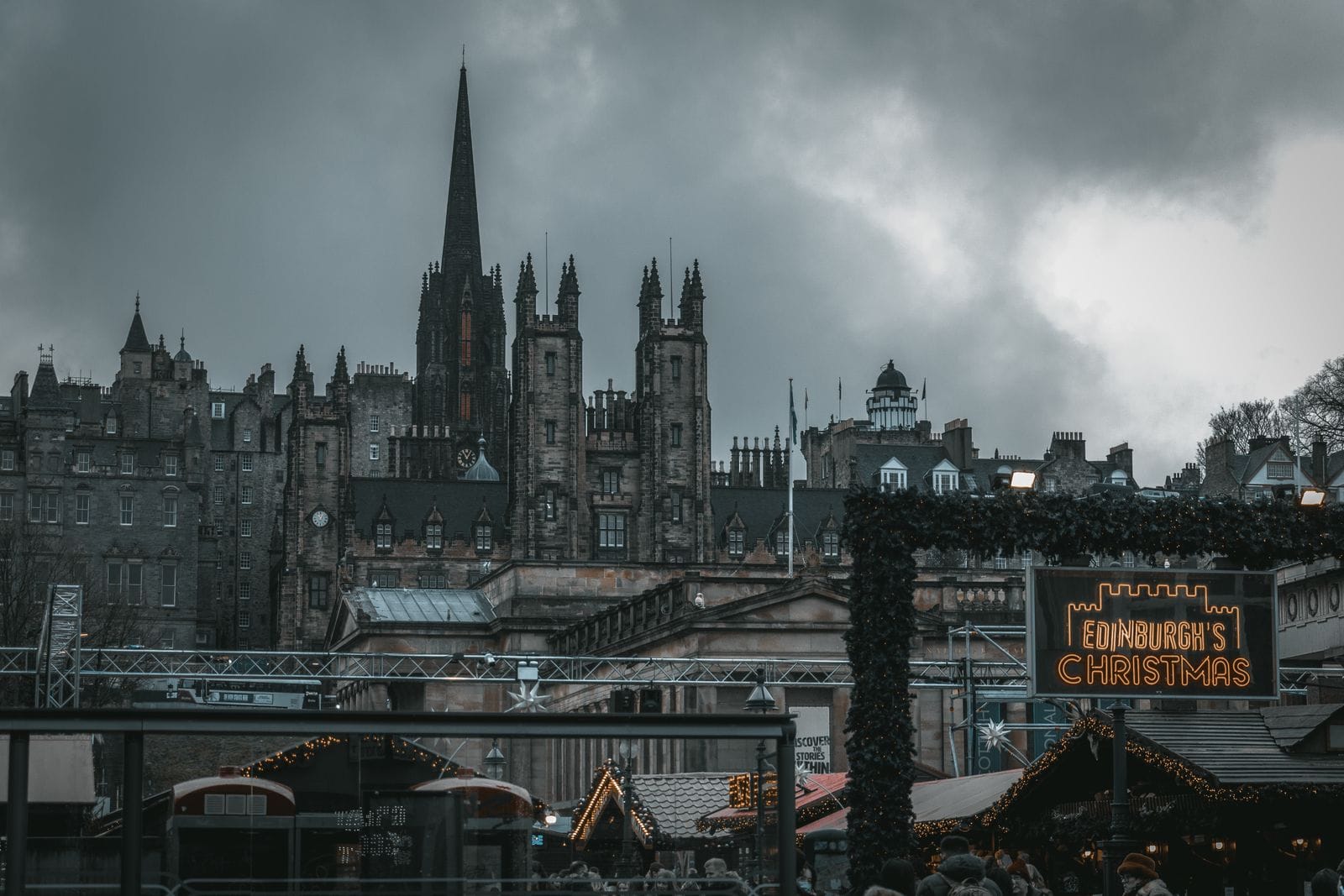 Best Christmas markets in the UK: the Edinburgh's Christmas sign beside market stalls, below the Old Town spires under a grey sky