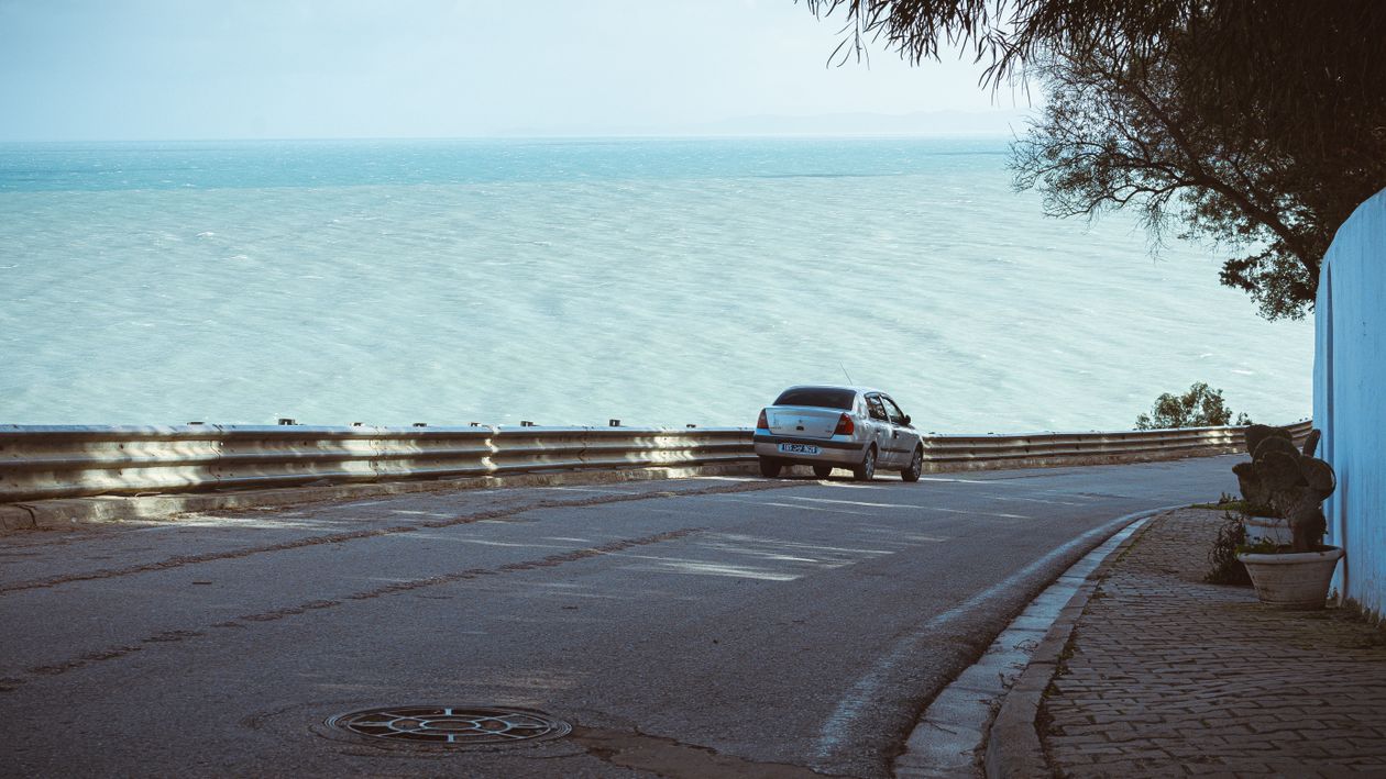 A silver car on a coastal road above the sea, the kind of holiday drive car hire excess insurance is bought for