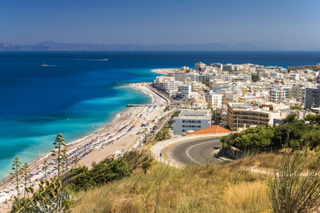 Cheapest Greek islands: the beach and seafront of Rhodes Town seen from a hillside, with the blue Aegean beyond